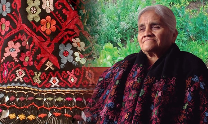 La imagen es un retrato de Manuela Cecilia Lino Bello, se encuentra sentada con una capa  de textil tradicional . reconocida con numerosos premios, ha dedicado décadas a la elaboración, preservación y promoción de tejidos y bordados de lana con tintes naturales. Desde los siete años, bajo la guía de su abuela, aprendió el arte textil tradicional, comprometiéndose a rescatar técnicas sostenibles como el añil y la cochinilla.